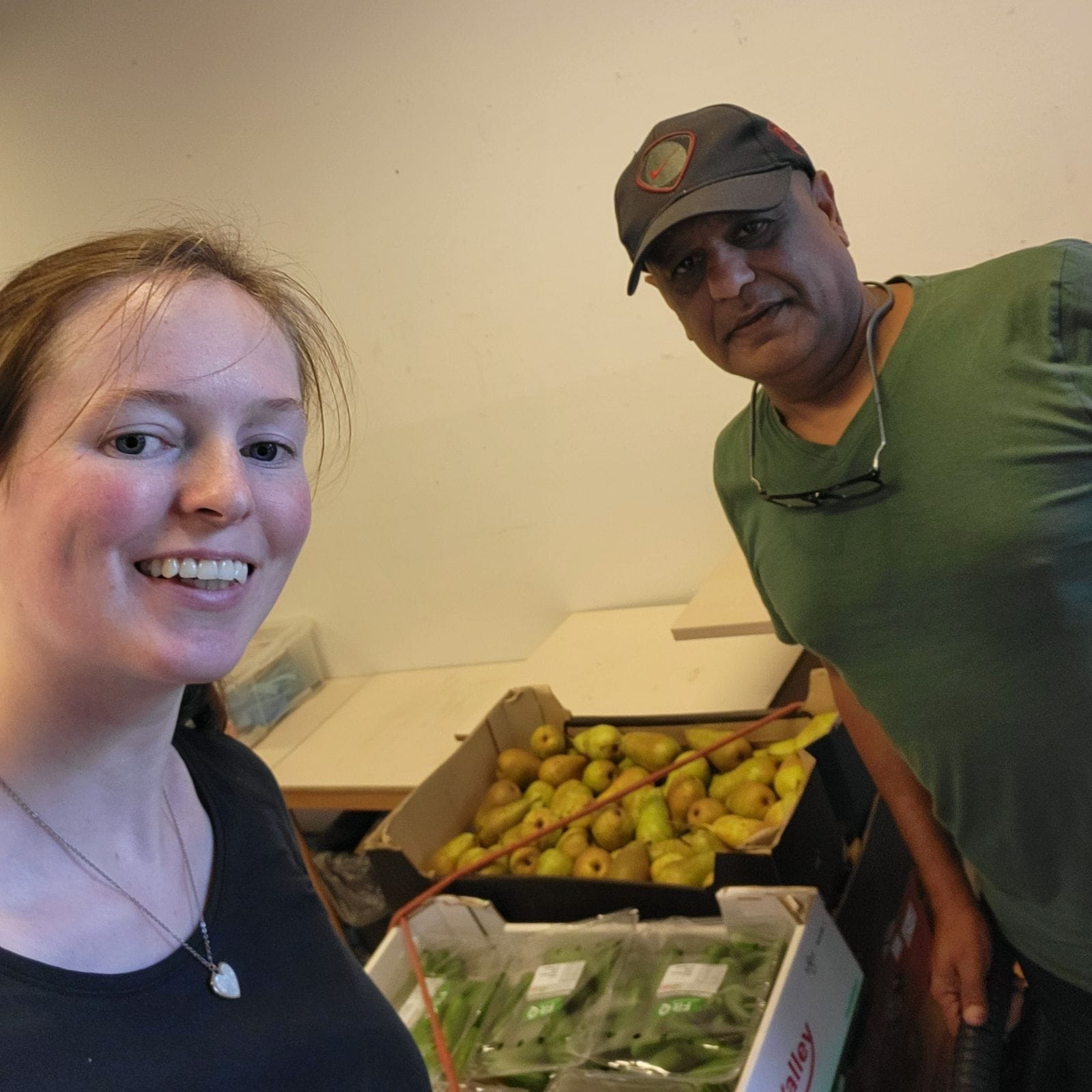 Twee mensen poseren naast dozen met peren en groenten.