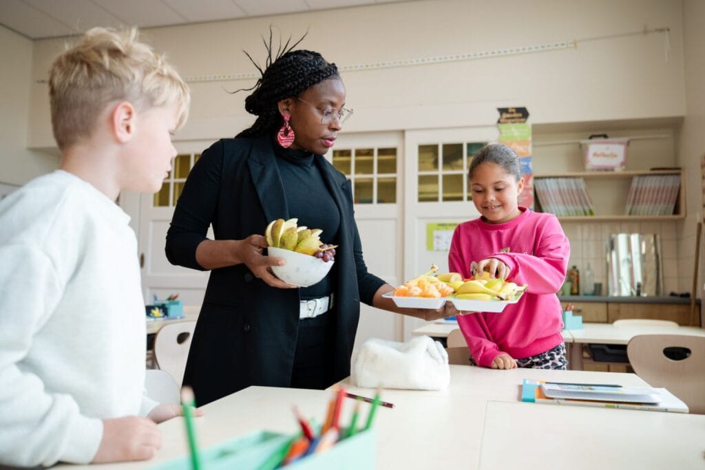 Lerares deelt fruit uit aan leerlingen in klas