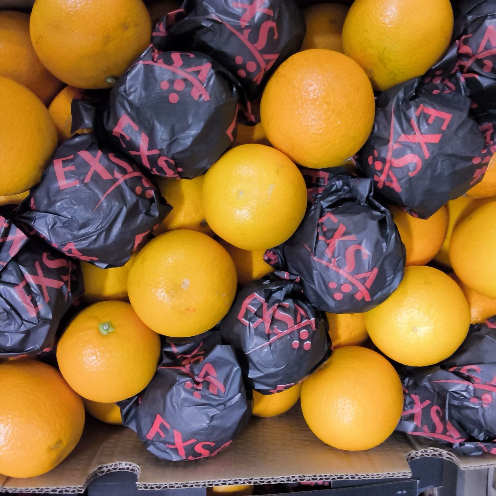Sinaasappels tussen zwarte Exsa-verpakkingen in een krat